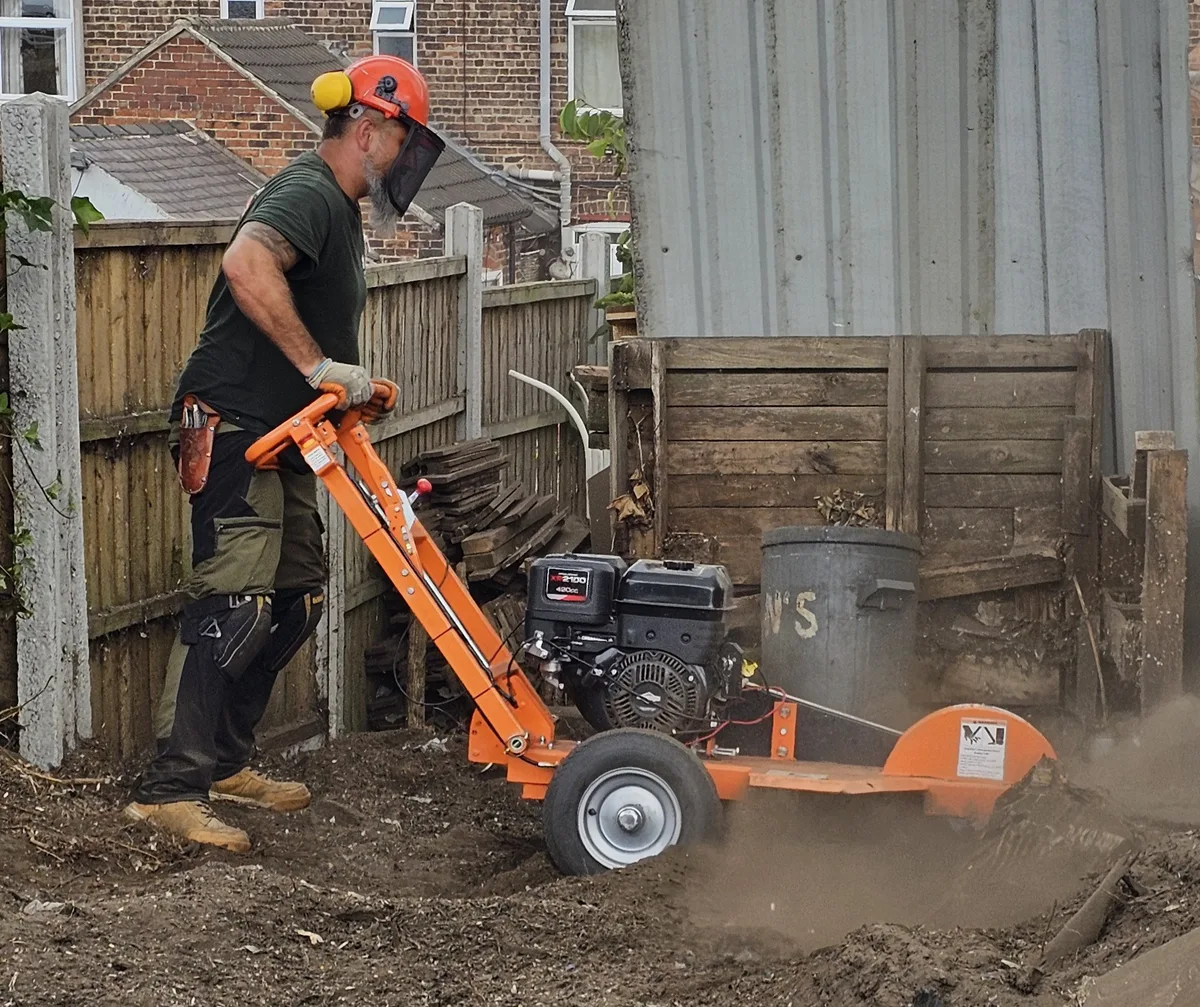Worker using a stump grinder to remove a tree stump in a garden